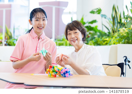 照顧畫面:一位老婦人在照顧者的陪伴下摺紙。攝影協助:東京電子電波學園大學 照顧畫面:一位老婦人在照顧者的陪伴下摺紙。攝影協助:東京電子電波學園大學 141878519