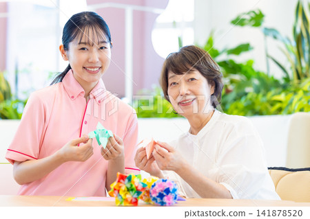 照顧畫面:一位老婦人在照顧者的陪伴下摺紙。攝影協助:東京電子電波學園大學 照顧畫面:一位老婦人在照顧者的陪伴下摺紙。攝影協助:東京電子電波學園大學 141878520