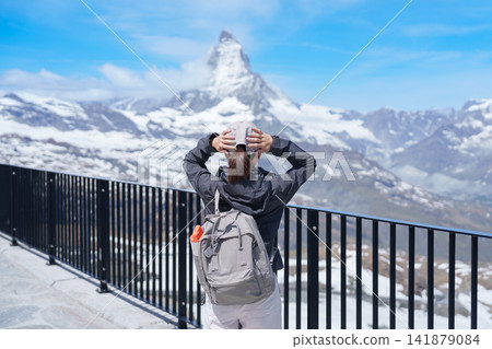 Woman Tourist Exploring Zermatt, Switzerland. happy Traveler sightseeing iconic Matterhorn Swiss Alps Viewpoint, Famous European Landmark, Popular Tourist Attraction and Travel Destination in Europe 141879084