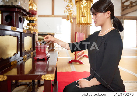 A scene from a Buddhist memorial service where a woman offers incense in front of the Buddha. A scene from a Buddhist memorial service where a woman offers incense in front of the Buddha. 141879276