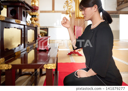 A scene from a Buddhist memorial service where a woman offers incense in front of the Buddha. A scene from a Buddhist memorial service where a woman offers incense in front of the Buddha. 141879277