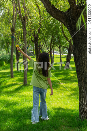 A young girl holding flowers walks away into a sunny forest path filled with tall green trees. A young girl holding flowers walks away into a sunny forest path filled with tall green trees. 141880000