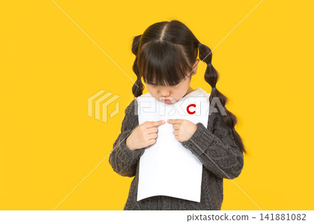 Little schoolgirl looking at her test paper with a bad grade C and feeling sad. Little schoolgirl looking at her test paper with a bad grade C and feeling sad. 141881082