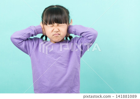 Frustrated little girl covering her ears with hands and closing eyes on a turquoise background. Frustrated little girl covering her ears with hands and closing eyes on a turquoise background. 141881089