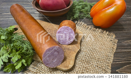 Traditional smoked sausage with fresh dill and tomatoes on a rustic wooden table. 141881180