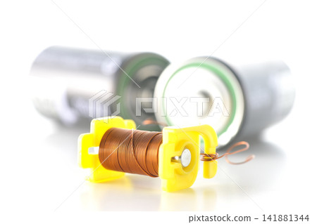A coil and a dry cell battery are photographed against a white background. A coil and a dry cell battery are photographed against a white background. 141881344