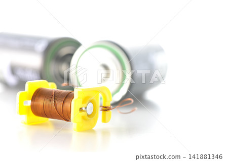 A coil and a dry cell battery are photographed against a white background. A coil and a dry cell battery are photographed against a white background. 141881346