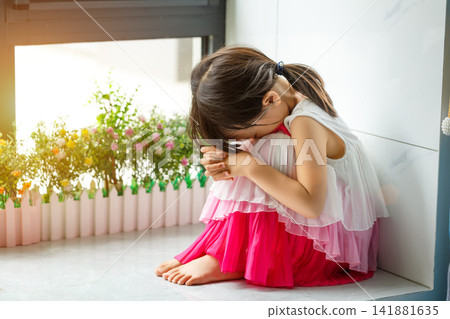 Sad and lonely little girl sitting on the floor in the corner looking depressed 141881635