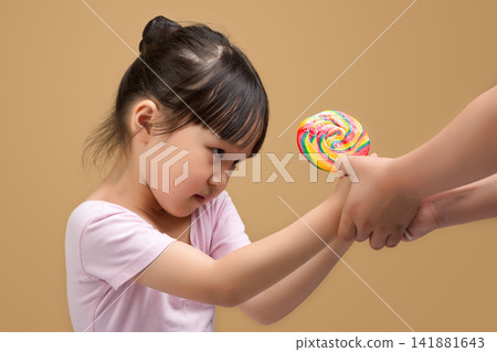 Little girl fighting over a colorful lollipop from a stranger or parent, healthy lifestyle 141881643