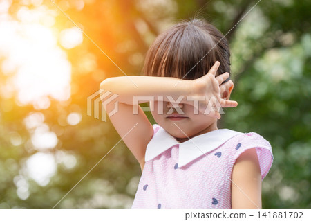 A lonely and heartbroken Asian little girl outdoors, covering her eyes with both hands. A lonely and heartbroken Asian little girl outdoors, covering her eyes with both hands. 141881702