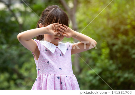 A lonely and heartbroken Asian little girl outdoors, covering her eyes with both hands. 141881703