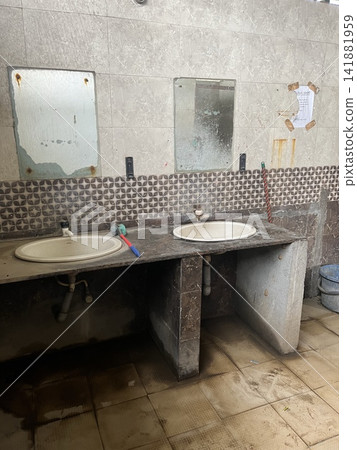 A handwashing area with a stone-patterned counter and two washbasins, a mirror mounted on the wall, and cleaning supplies. A handwashing area with a stone-patterned counter and two washbasins, a mirror mounted on the wall, and cleaning supplies. 141881959