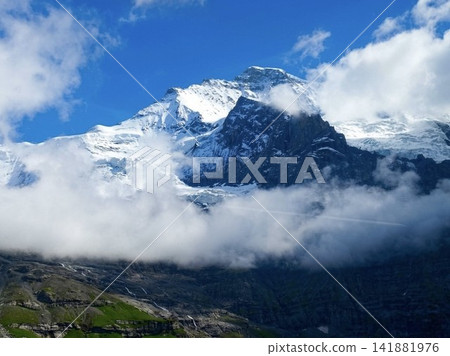 The majestic snow-capped mountains rise proudly above the sea of clouds in the Swiss Alps, against a clear blue sky. The majestic snow-capped mountains rise proudly above the sea of clouds in the Swiss Alps, against a clear blue sky. 141881976
