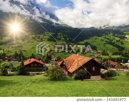 The lush mountain village of Grindelwald, Switzerland, bathed in sunlight, and the scenery of traditional wooden mountain lodges. The lush mountain village of Grindelwald, Switzerland, bathed in sunlight, and the scenery of traditional wooden mountain lodges. 141881977