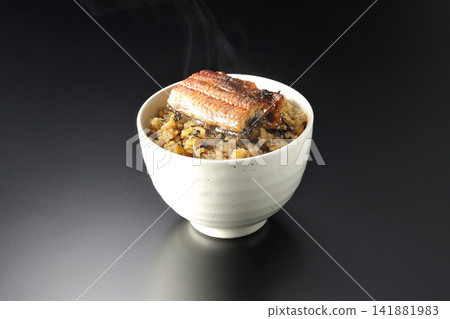 A piping hot mini eel rice bowl photographed alone against a black background. A piping hot mini eel rice bowl photographed alone against a black background. 141881983