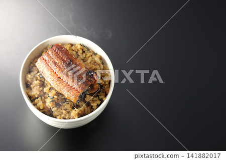 A piping hot mini eel rice bowl photographed alone against a black background. A piping hot mini eel rice bowl photographed alone against a black background. 141882017
