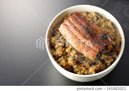 A piping hot mini eel rice bowl photographed alone against a black background. A piping hot mini eel rice bowl photographed alone against a black background. 141882021
