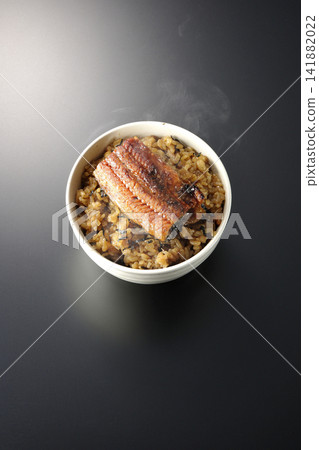 A piping hot mini eel rice bowl photographed alone against a black background. A piping hot mini eel rice bowl photographed alone against a black background. 141882022