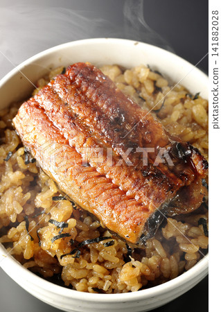 A piping hot mini eel rice bowl photographed alone against a black background. A piping hot mini eel rice bowl photographed alone against a black background. 141882028