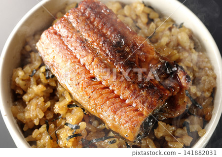 A piping hot mini eel rice bowl photographed alone against a black background. A piping hot mini eel rice bowl photographed alone against a black background. 141882031
