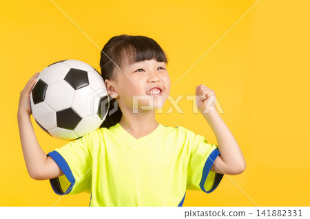 A high-energy portrait of the same East Asian girl on a solid yellow backdrop, holding the soccer ball aloft with one hand while cheering excitedly and raising her other fist in a victorious gesture, A high-energy portrait of the same East Asian girl on a solid yellow backdrop, holding the soccer ball aloft with one hand while cheering excitedly and raising her other fist in a victorious gesture, 141882331