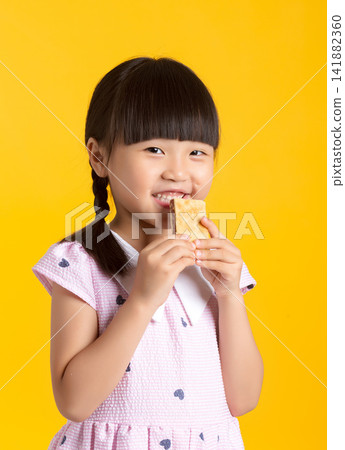 Happy smiling girl holding a crispy wafer biscuit with both hands on yellow background 141882360