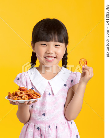 Happy child showing a piece of dehydrated fruit snack while holding a plate 141882369