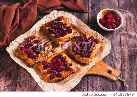 Raspberry and sugar topping on square puff pastry tarts on a board on a table Raspberry and sugar topping on square puff pastry tarts on a board on a table 141882679
