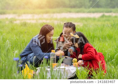 Family picnic on the grass with fruits and drinks, mother and children eating together. Family picnic on the grass with fruits and drinks, mother and children eating together. 141883407