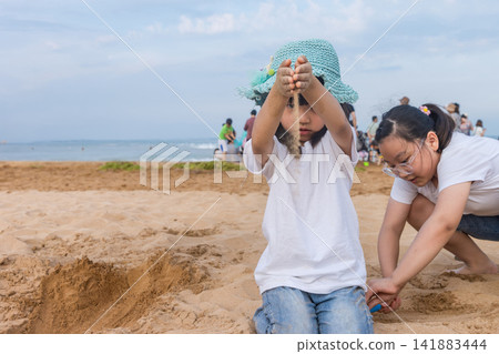 Asian Little Girl Playing With Sand on Beach During Summer Vacation Asian Little Girl Playing With Sand on Beach During Summer Vacation 141883444