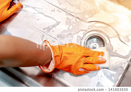 Housekeeper hand wearing orange rubber glove scrubbing on kitchen sink drainer Housekeeper hand wearing orange rubber glove scrubbing on kitchen sink drainer 141883830