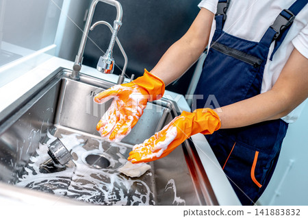 Housekeeper showing hands with rubber glove full with soap suds while scrubbing on kitchen sink Housekeeper showing hands with rubber glove full with soap suds while scrubbing on kitchen sink 141883832
