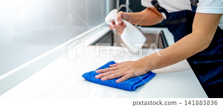Male housekeeper hand holding spray bottle while wiping microfiber cloth on white countertop Male housekeeper hand holding spray bottle while wiping microfiber cloth on white countertop 141883836