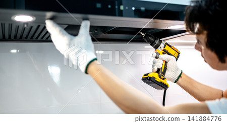 Asian male technician using electric screwdriver fixing extractor motor in cooker hood Asian male technician using electric screwdriver fixing extractor motor in cooker hood 141884776
