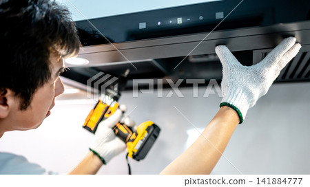 Asian male technician using electric screwdriver fixing extractor motor in cooker hood Asian male technician using electric screwdriver fixing extractor motor in cooker hood 141884777