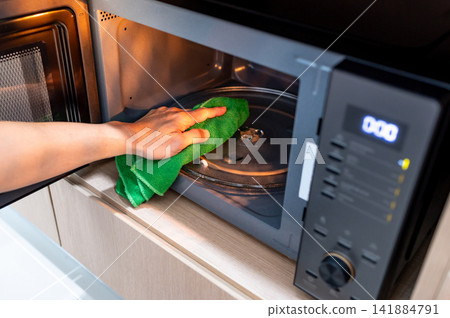 Male hand holding green microfiber cloth wiping inside the black microwave oven Male hand holding green microfiber cloth wiping inside the black microwave oven 141884791