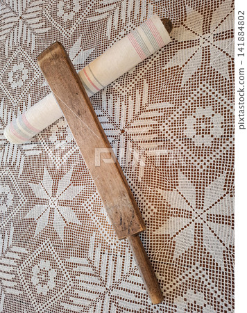 Vintage wooden mangle board rests on a lace tablecloth next to a rolled textile used for ironing clothes Vintage wooden mangle board rests on a lace tablecloth next to a rolled textile used for ironing clothes 141884802