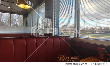 A classic American diner interior with red leather sofas and a wooden table. Large louvered windows overlook the street. A classic American diner interior with red leather sofas and a wooden table. Large louvered windows overlook the street. 141884966