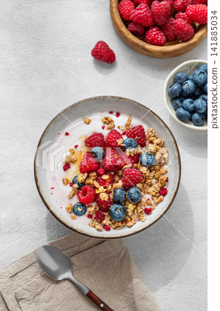 Natural greek yogurt with granola, blueberry and raspberry in a bowl on a light concrete background Natural greek yogurt with granola, blueberry and raspberry in a bowl on a light concrete background 141885034