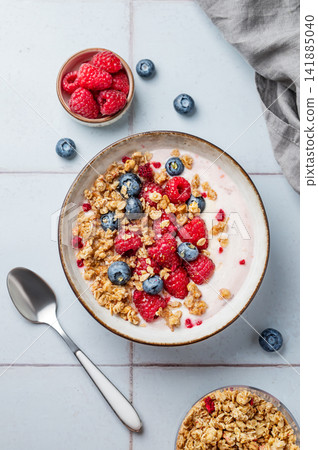 Natural greek yogurt with granola, blueberry and raspberry in a bowl on a blue tile background Natural greek yogurt with granola, blueberry and raspberry in a bowl on a blue tile background 141885040