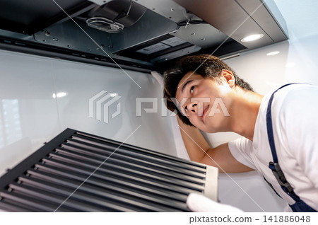 Asian male technician removing range metal filter looking inside the cooker hood Asian male technician removing range metal filter looking inside the cooker hood 141886048