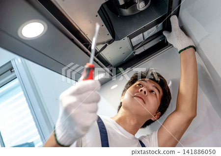 Asian male technician using screwdriver fixing extractor motor in cooker hood Asian male technician using screwdriver fixing extractor motor in cooker hood 141886050