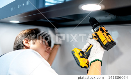 Asian male technician using electric screwdriver fixing extractor motor in cooker hood Asian male technician using electric screwdriver fixing extractor motor in cooker hood 141886054