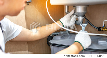 Male plumber with glove fixing pipe connection under the kitchen sink Male plumber with glove fixing pipe connection under the kitchen sink 141886055