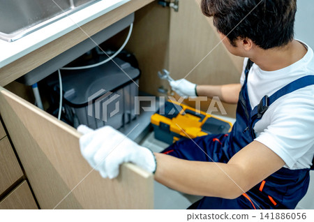 Asian male plumber checking pipe system under the kitchen sink Asian male plumber checking pipe system under the kitchen sink 141886056
