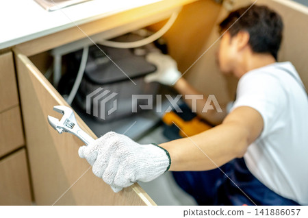 Asian male plumber checking pipe system under the kitchen sink Asian male plumber checking pipe system under the kitchen sink 141886057