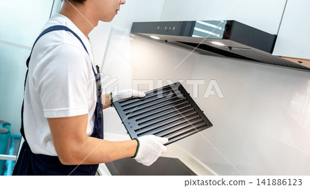 Asian male maintenance worker holding range hood filter in domestic kitchen Asian male maintenance worker holding range hood filter in domestic kitchen 141886123