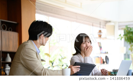 A man and woman are chatting happily in an office where people are working on their computers. A man and woman are chatting happily in an office where people are working on their computers. 141886459