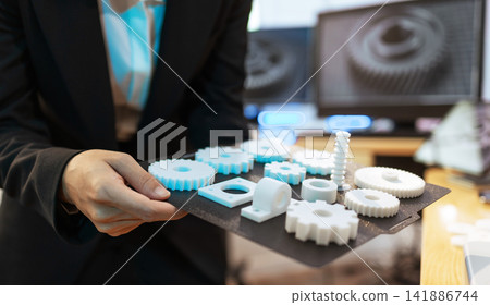 Business person holding a tray of 3d printed gears and parts in an office, engineering, prototyping and manufacturing work. Business person holding a tray of 3d printed gears and parts in an office, engineering, prototyping and manufacturing work. 141886744