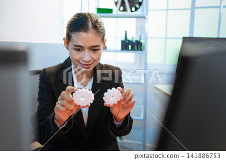Businesswoman holding two gears in an office, teamwork, planning and business process concept. Businesswoman holding two gears in an office, teamwork, planning and business process concept. 141886753